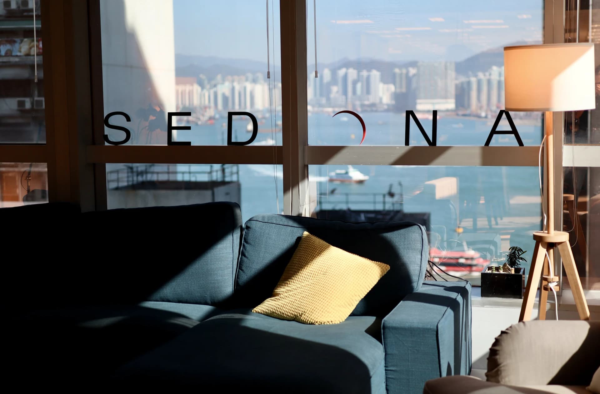 Sedona Hong Kong office lounge, sofa beside the SEDONA wordmark on the window with Victoria Harbour beyond.